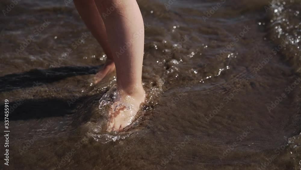 the legs of a young child walk along the beach in the waves of the ocean. family holidays with parents. the legs of a young child walk along the beach in the waves of the ocean. family holidays with parents.