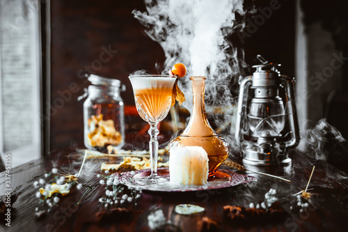 Side view of an unusual yellow sour smokey cocktail in a glass on a wooden table with decorative elements, horizontal format