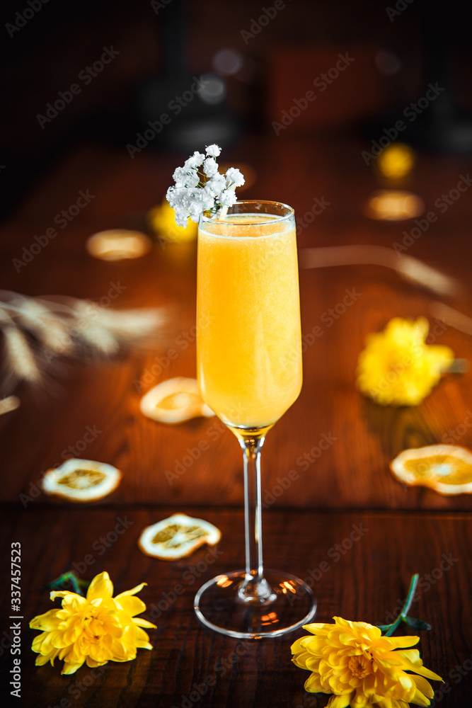 Side view of delicious sweet yellow alcohol cocktail in champagne glass on the wooden table with yellow flowers as decorative elements, vertical
