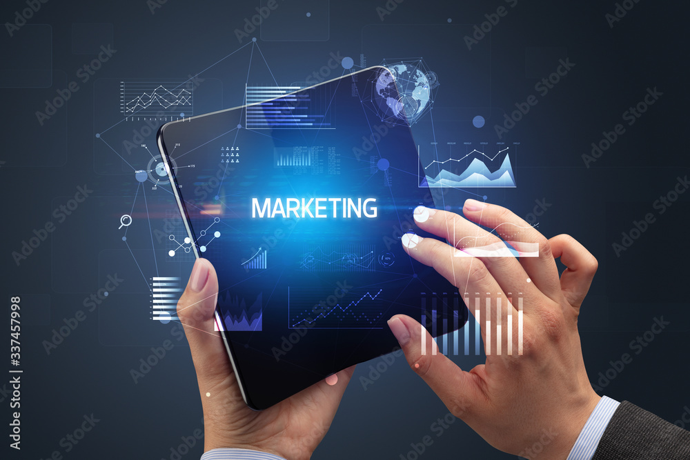 Businessman holding a foldable smartphone with MARKETING inscription, successful business concept