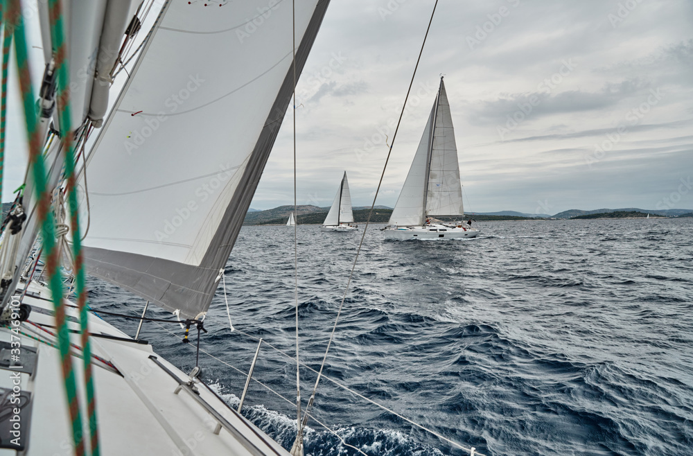 Naklejka premium Croatia, Adriatic Sea, 19 September 2019: The race of sailboats, the team sits on the edge of a boat board, bright colors, view of participants of race from other boat through ropes and sails