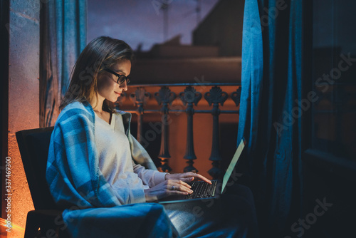 Home Office Late At Night, Young female professional copywritter in chair working at home, businesswoman working at night in homewear and eyeglasses using laptop computer reading email from client photo