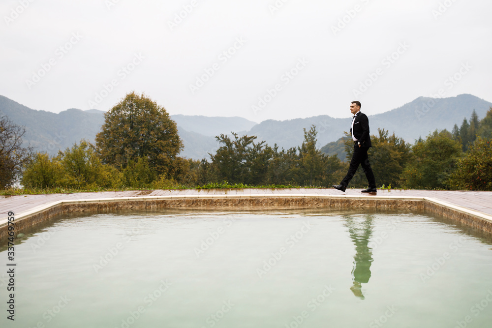 Man dressed in business festive costume standing by the pool alone in autumn