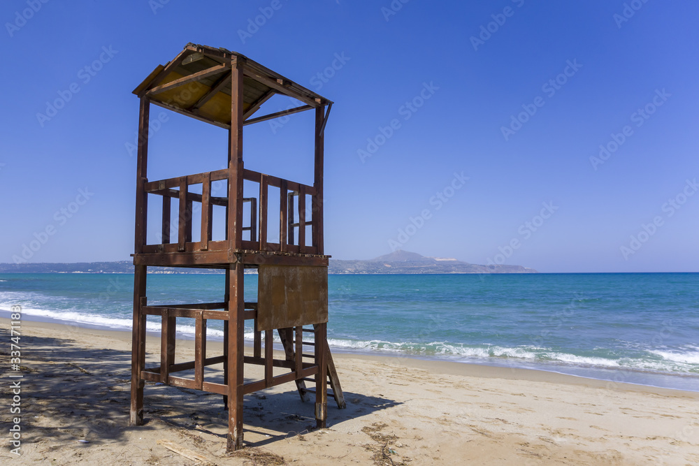Empty wooden lifeguard tower on sandy beach without tourists as concept of low season. Bright blue and calm sea with distant mountains, beautiful view.