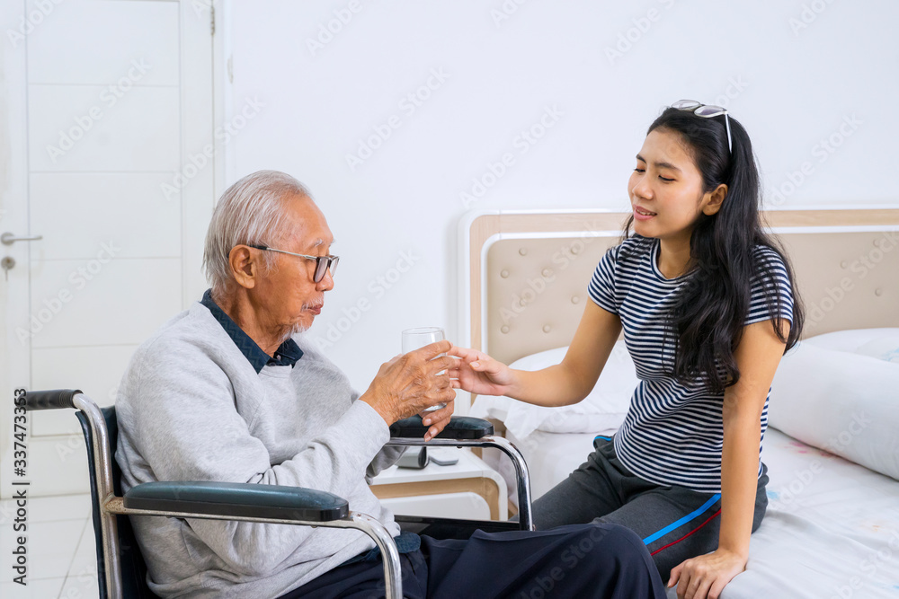 Young woman giving water to her father in bedroom Young woman giving water to her father in bedroom