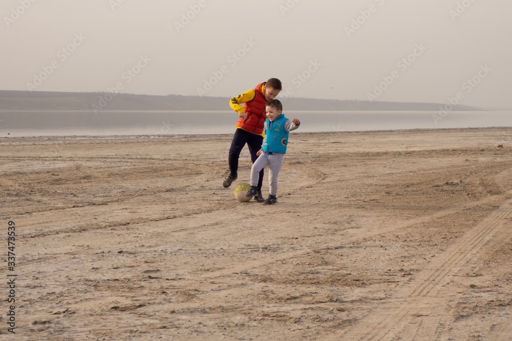 Two brothers 10 and 4 years old play soccer on an empty beach. Two brothers 10 and 4 years old play soccer on an empty beach.