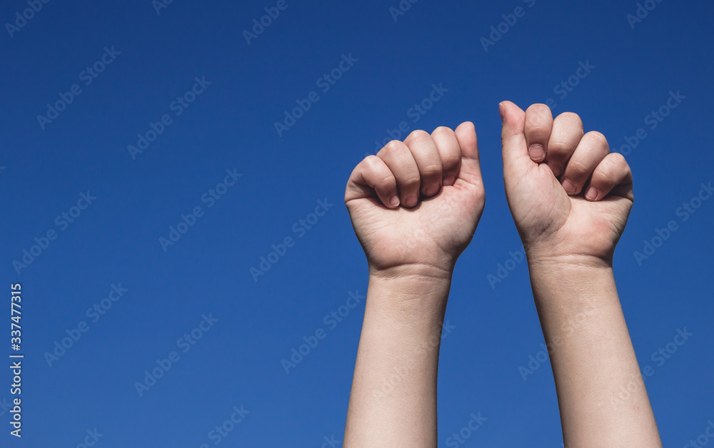 Children's fists raised up showing power. Kid's hands raised against the clear blue sky, symbol of resistance movement. Body parts concept, close up, gradient background, copy empty space for text. Children's fists raised up showing power. Kid's hands raised against the clear blue sky, symbol of resistance movement. Body parts concept, close up, gradient background, copy empty space for text.