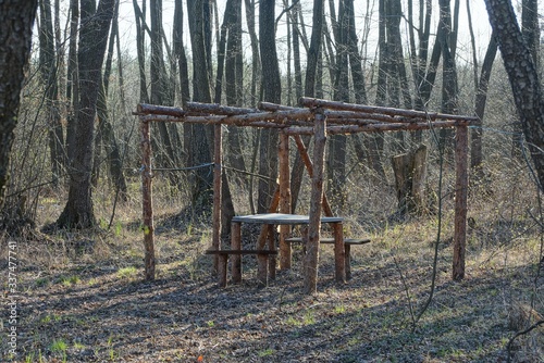 old brown wooden arbor with a table and benches in the grass among the trees in the forest
