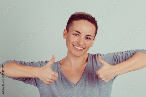 Enthusiastic motivated woman giving a thumbs up gesture of approval and success isolated on light green gray background