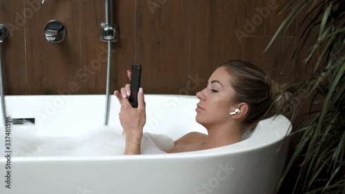 Girl at home in bath with relax listens to music on headphones from the phone