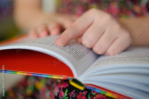 Little girl in a colorful dress is reading a book. Child learns to read.