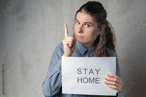 A young girl with an inscription on a sheet of paper calls for quarantine to stay at home. Home self-isolation in pandemic, flu epidemic, viral diseases, Covid-19.