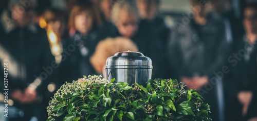 A metal urn with ashes of a dead person on a funeral, with people mourning in the background on a memorial service. Sad grieving moment at the end of a life. Last farewell to a person in an urn. photo
