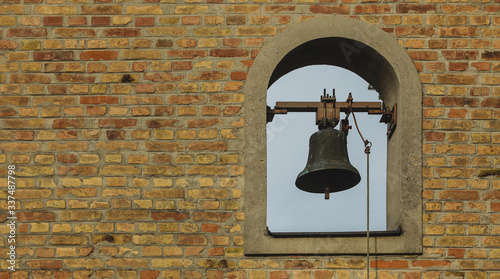 Tower bell of a small brick made church. Bell is seen inside an opening in a brick wall.