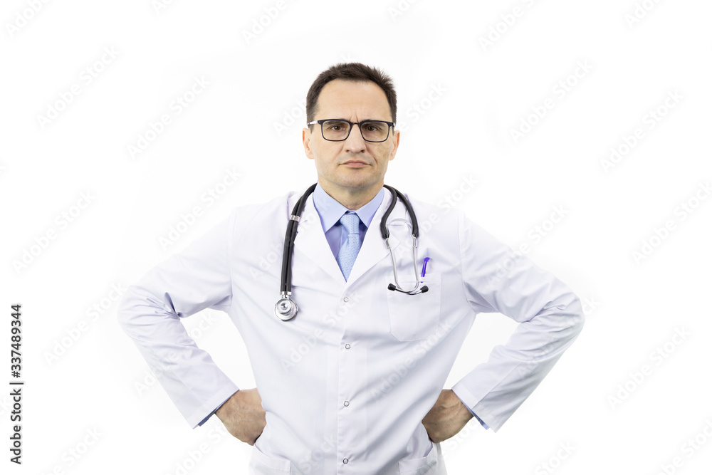 The therapist with glasses in a white coat with a stethoscope stands on a white background and looks at the camera. Hands on hips. Medical worker. Serious look. Portrait of a doctor. The therapist with glasses in a white coat with a stethoscope stands on a white background and looks at the camera. Hands on hips. Medical worker. Serious look. Portrait of a doctor.