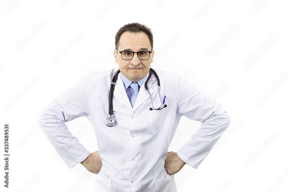 Fototapeta premium Middle-aged handsome doctor in white coat, glasses and stethoscope looking at camera with anger face with hands on sides, isolated white background. healthcare, negative emotions and medicine concept