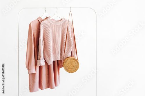 Feminine pale pink warm sweater and dress with bamboo bag on hanger on white background. Elegant   fashion outfit. Spring wardrobe. Minimal concept. photo