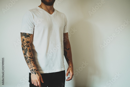 Cropped photo of a tattooed man dressed in casual clothes demonstrating an empty place for design on a white blank t-shirt. Horizontal mockup.