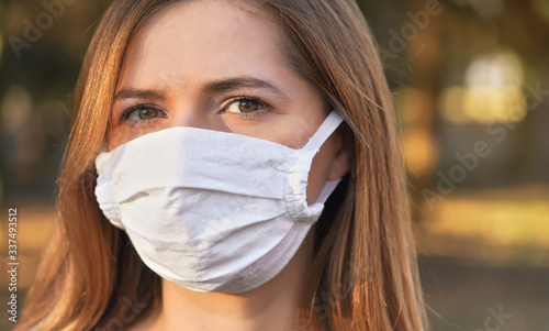 Young woman wearing white cotton virus mouth nose mask, nice bokeh in background, closeup face portrait