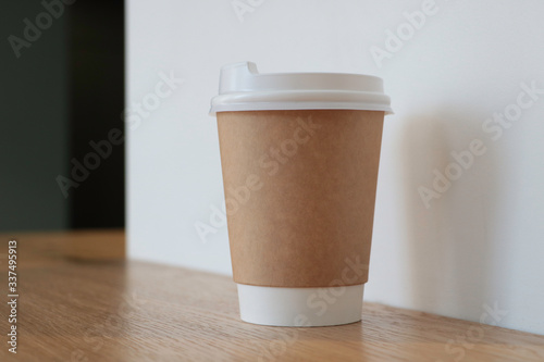 Mock up with a cup of coffee. A glass is on the table in a cafe  selling coffee in the background. Coffee to go. Light walls. Wooden table. Cafe. Disposable cup