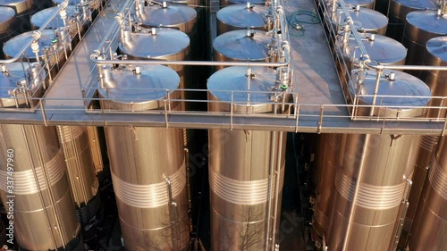 Rows of tall stainless steel tanks connected with pipes. Shiny silos in a chemical industry plant. Metal containers with hazardous chemicals. Aerial footage.