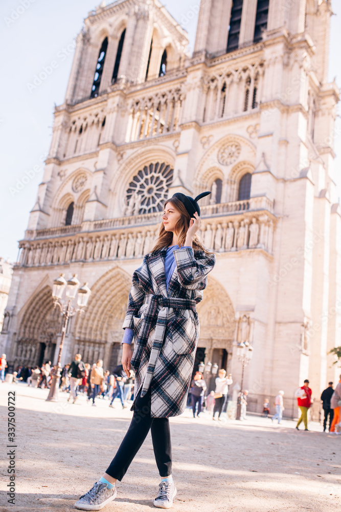 girl in a mikimaus hat in a beautiful coat on the background of the Parisian Cathedral of Notre Dame