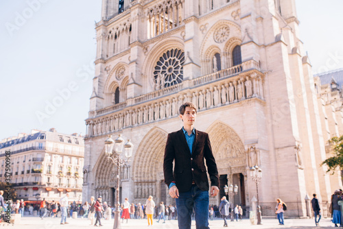 a young man poses against the backdrop of Notre Dame Cathedral in Paris.