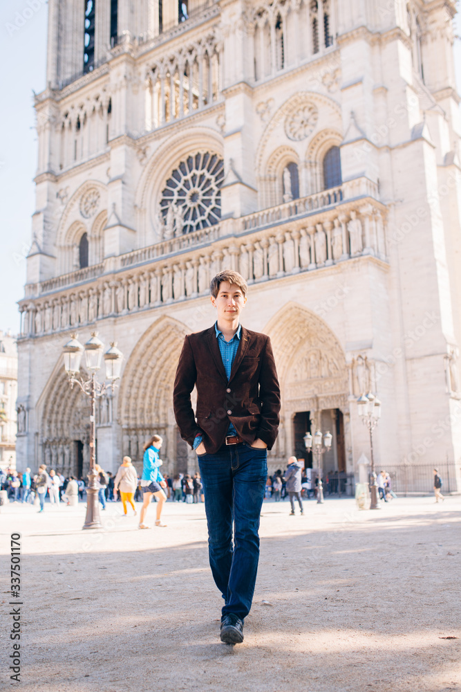 a young man poses against the backdrop of Notre Dame Cathedral in Paris.