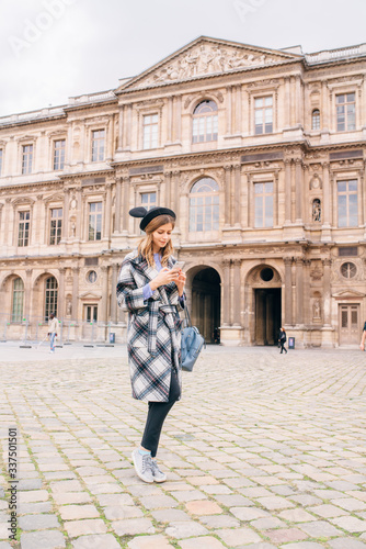 A girl in a beautiful coat stands near the Louvre.