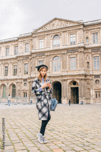 A girl in a beautiful coat stands near the Louvre.
