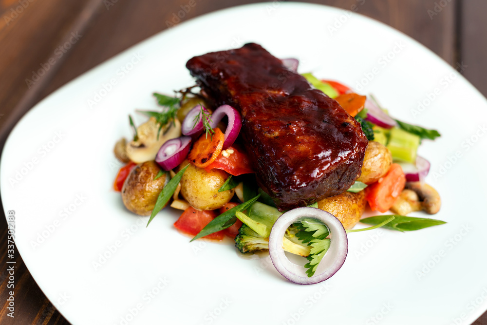 A calf steak with a young potato and juicy vegetables on a wooden background A calf steak with a young potato and juicy vegetables on a wooden background
