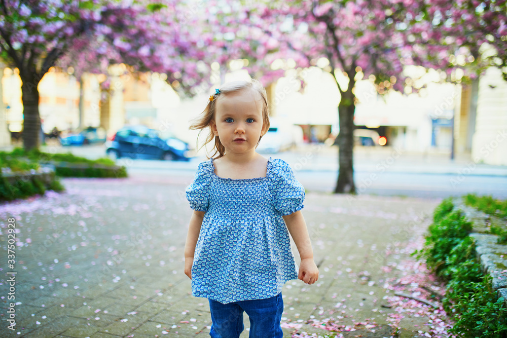 Cheerful two year old girl having fun in park with blooming cherry blossom trees Cheerful two year old girl having fun in park with blooming cherry blossom trees