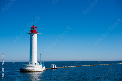 A lighthouse stands in the sea on the water. The blue sea is far away, the shore is not visible. Bright blue sky, blue water
