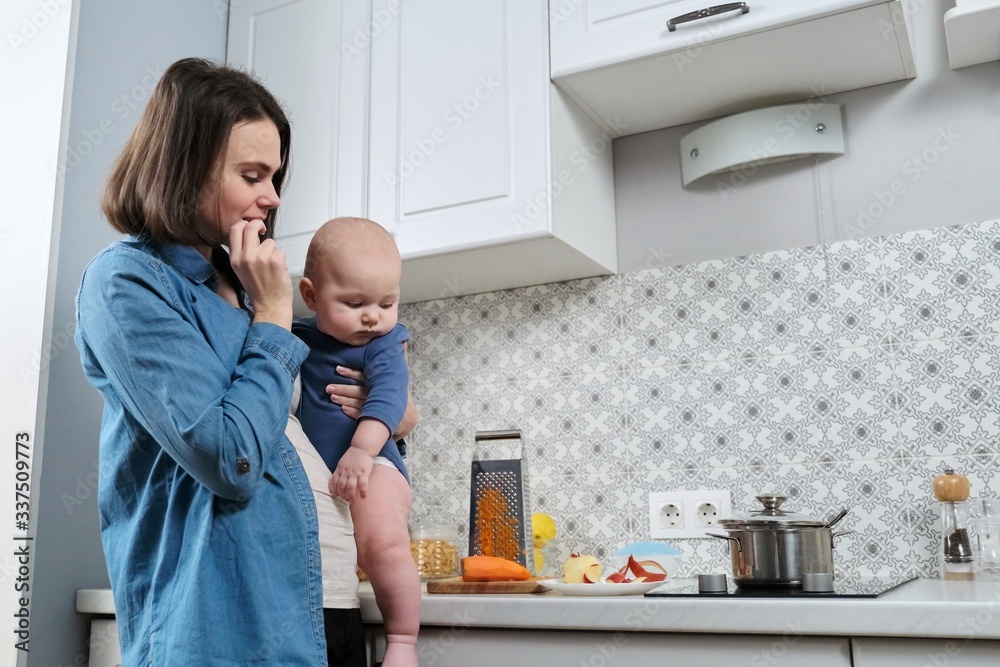 Obraz premium Young beautiful woman with baby in her arms in kitchen