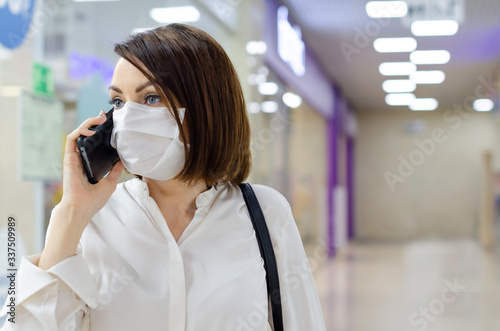  A woman in a medical mask on her face protecting from coronavirus is talking on the phone. Conservation concept from Covid-19.