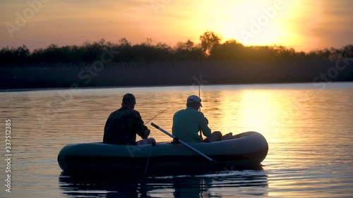 Two fishermen in the rays of the sunset catch fish from an inflatable boat