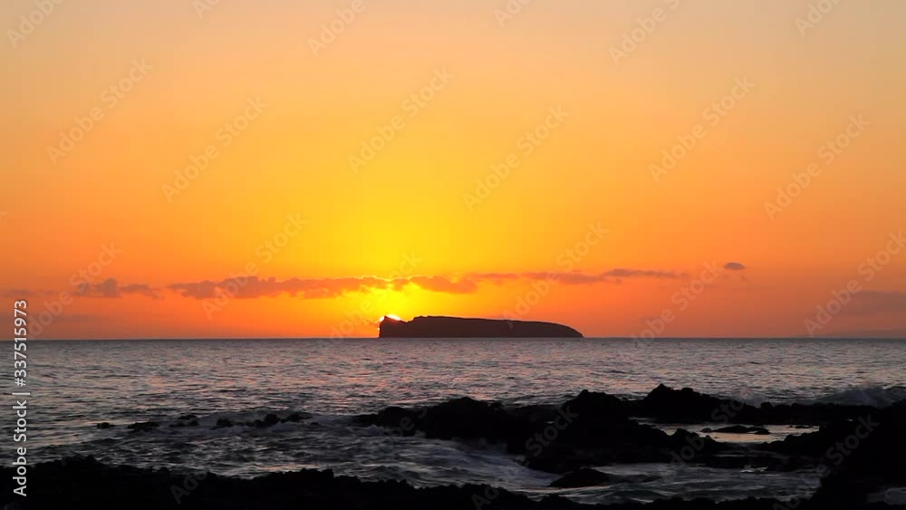 Sped up video of the sun setting behind Molokini Crater off the Maui shore with rich orange-colored sky and ocean waves rolling into shore is a dramatic tropical Hawaii visual. Sped up video of the sun setting behind Molokini Crater off the Maui shore with rich orange-colored sky and ocean waves rolling into shore is a dramatic tropical Hawaii visual.