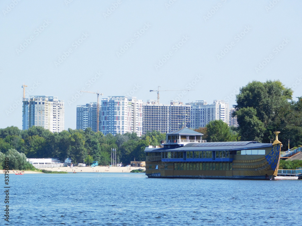 Fototapeta premium A floating restaurant on Dnipro river against the backdrop of buildings construction in Kyiv, Ukraine.