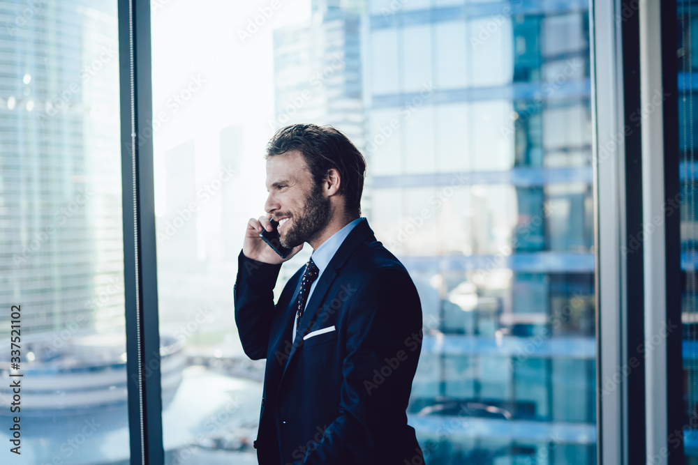 Cheerful bearded male entrepreneur in elegant formal wear having mobile phone conversation about business in office, successful man 30s manager joking talking on cellular near panoramic window Cheerful bearded male entrepreneur in elegant formal wear having mobile phone conversation about business in office, successful man 30s manager joking talking on cellular near panoramic window