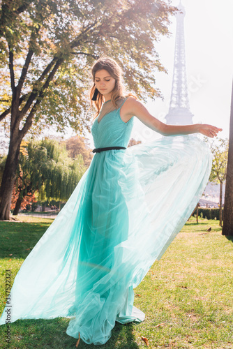 Beautiful girl in an azure evening dress in Paris with the Eiffel tower in the background.