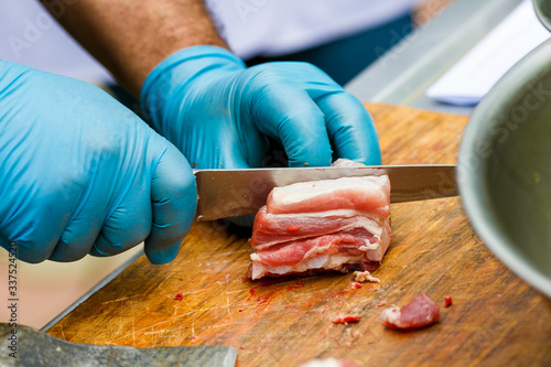 Close-up. A cook man in blue disposable gloves cuts a piece of red meat into pieces.