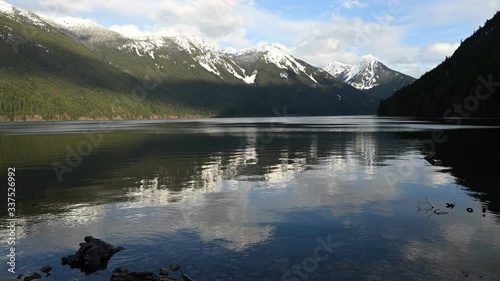 Chilliwack Lake with dead fallen tree trunks and driftwood in the foreground and the reflecting Mount Redoubt (Skagit Range Mountains) in the background.