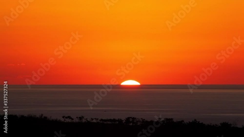 Sped-up video of an Hawaii sunset as seen from Pukalani on Maui with extra-deep orange and red sky and dark wave-rippled ocean in the distance. photo