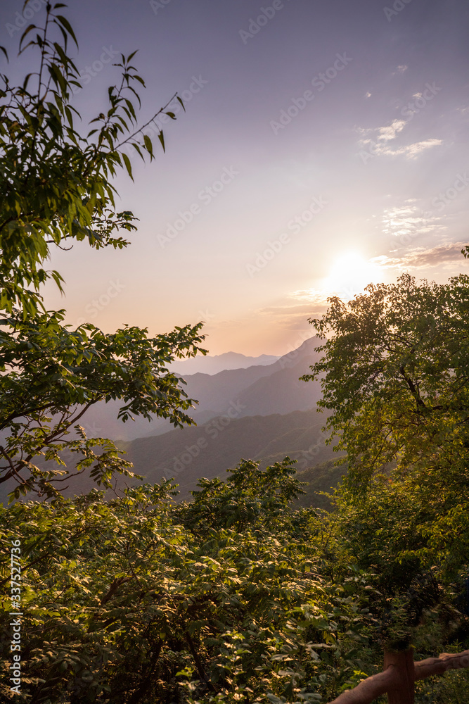 Beams of evening sunlight spill through the peaceful clouds over the mountains surrounding the Great Wall of China near Beijing, China. Beams of evening sunlight spill through the peaceful clouds over the mountains surrounding the Great Wall of China near Beijing, China.