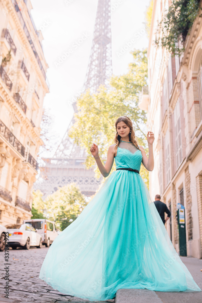 Obraz premium Beautiful young girl in a dress on the street with a view of the Eiffel tower