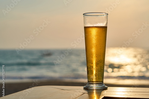 Glass of a cold beer at sunset, sea and beach in the background.