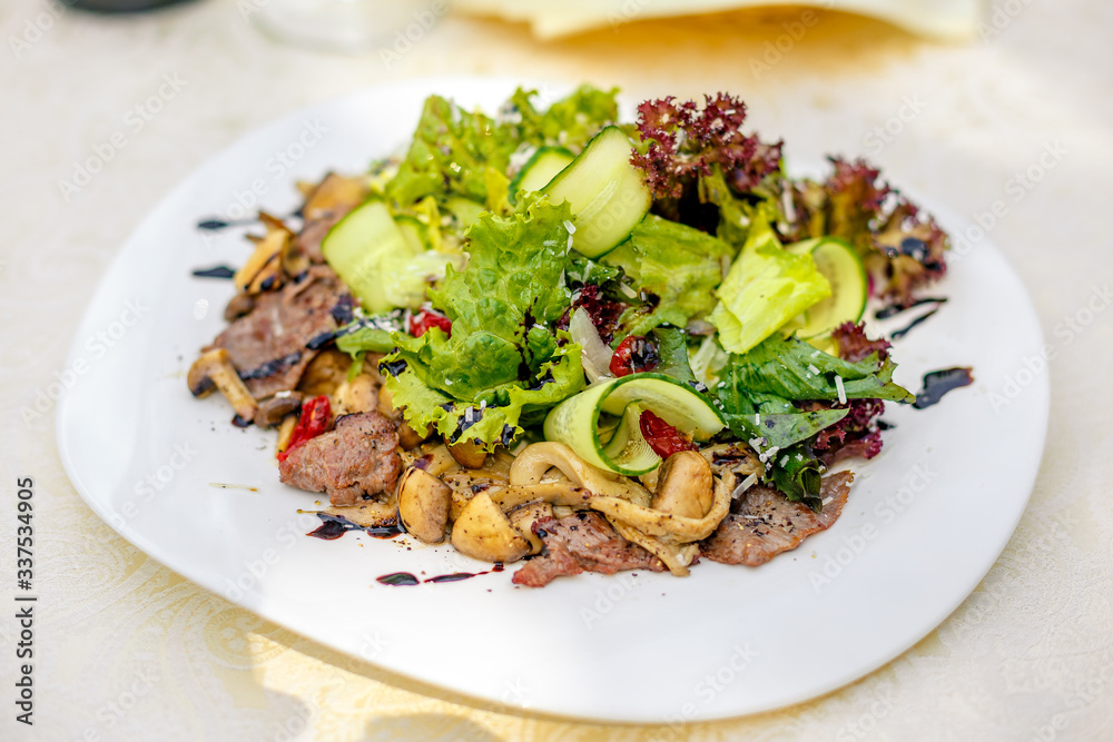 warm salad with meat, cucumber and vegetables on a white plate on the table warm salad with meat, cucumber and vegetables on a white plate on the table