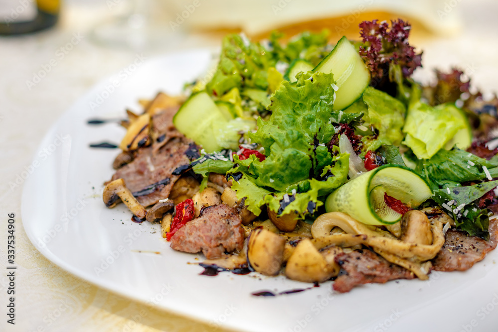warm salad with meat, cucumber and vegetables on a white plate on the table