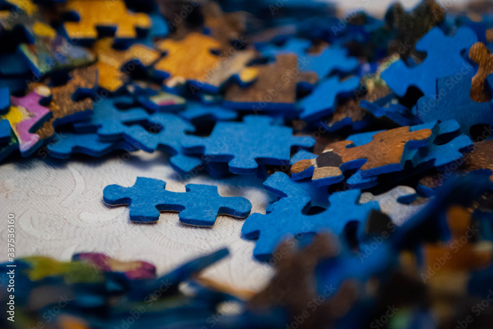 Close-up of colorful pieces of puzzle. One standing puzzle piece on the table. Stack of Puzzle Pieces. Puzzle pieces. Puzzle figures. Puzzle for fun.  - obrazy, fototapety, plakaty 