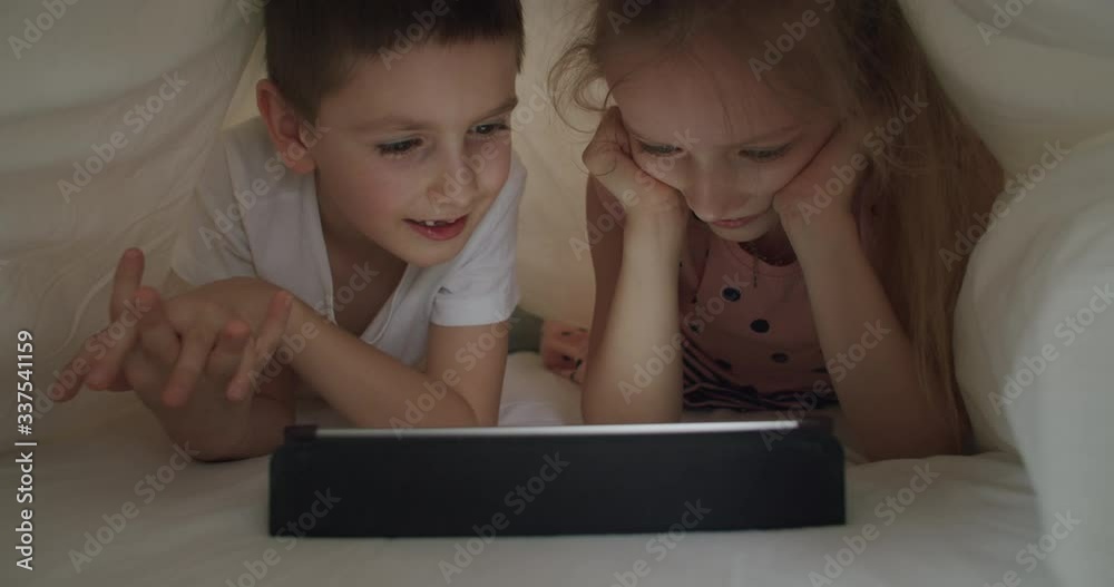 boy and girl lying under blanket with tablet